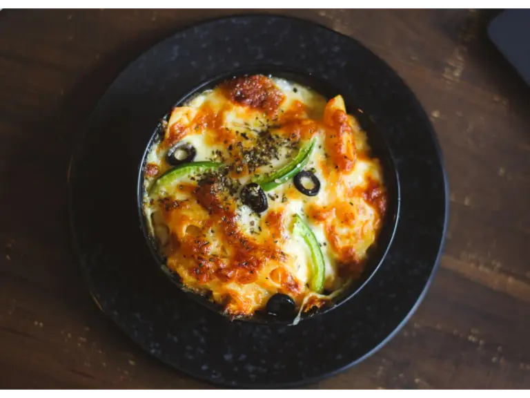 a serving of baked ziti pasta sitting on a black plate, topped with melted cheese, tomato sauce, and fresh herbs for a flavorful presentation.