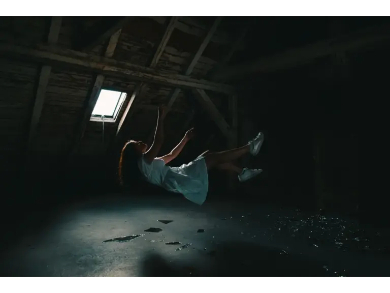A surreal photograph of a woman in a white dress floating in an abandoned attic, capturing a mysterious vibe inspired by falling dreams.