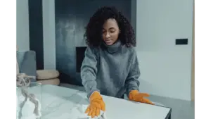 A woman wearing gloves wipes a table in a cozy modern living room, capturing the calm, satisfying rhythm of everyday home cleaning.