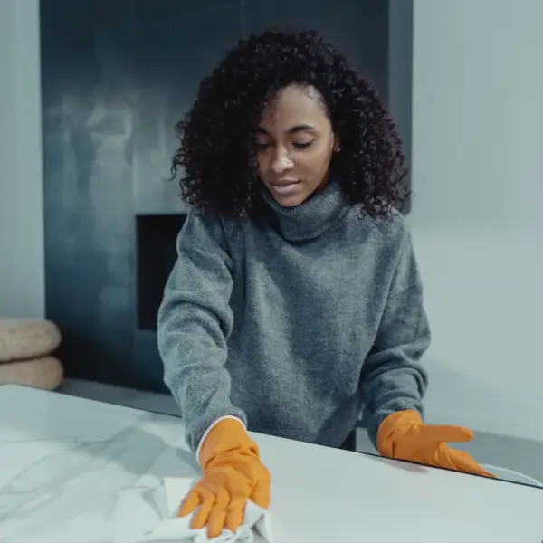 A woman wearing gloves wipes a table in a cozy modern living room, capturing the calm, satisfying rhythm of everyday home cleaning.