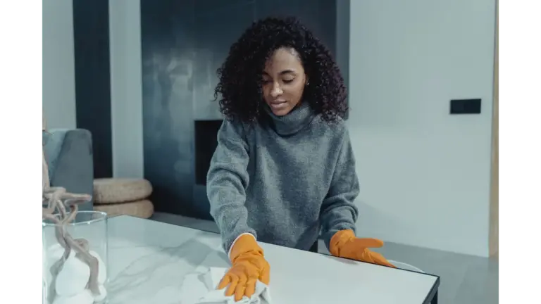 A woman wearing gloves wipes a table in a cozy modern living room, capturing the calm, satisfying rhythm of everyday home cleaning.
