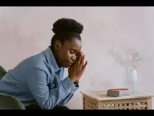 For a daily devotional for women, a woman prays at home while sitting beside a small table.
