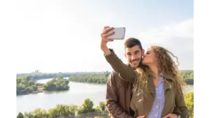 A happy couple enjoys a moment by the river, capturing a selfie to cherish their travel memories during a sweet couples travel getaway.