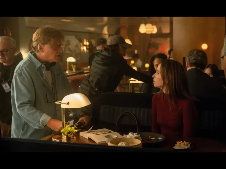 A scene in a restaurant from The Social Reckoning with a male director talking to a female actor, while other people are seen in the background.