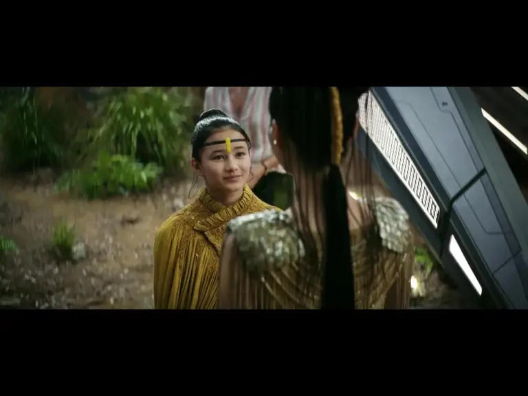 Kaylee Hottle in Godzilla X Kong: The New Empire (2024), with a yellow outfit and a headband, speaks to an adult woman in a dramatic setting.