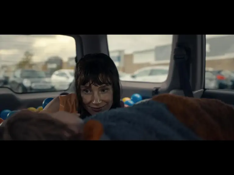 Jessica Chastain in Other Mommy (2026) smiles while leaning over a figure who appears to be lying down in the backseat of a car filled with colorful balls.