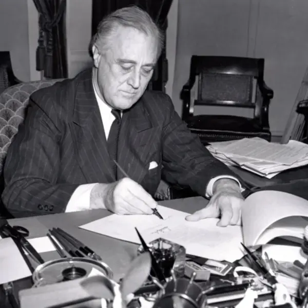 President Franklin D. Roosevelt, half-length portrait, seated at desk, looking down, signing H.R. 1776, the lend-lease bill to give aid to Great Britain, China and Greece.