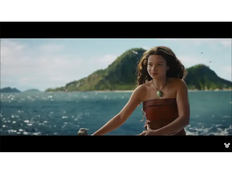 Moana sailing through ocean with a mountain in the background.