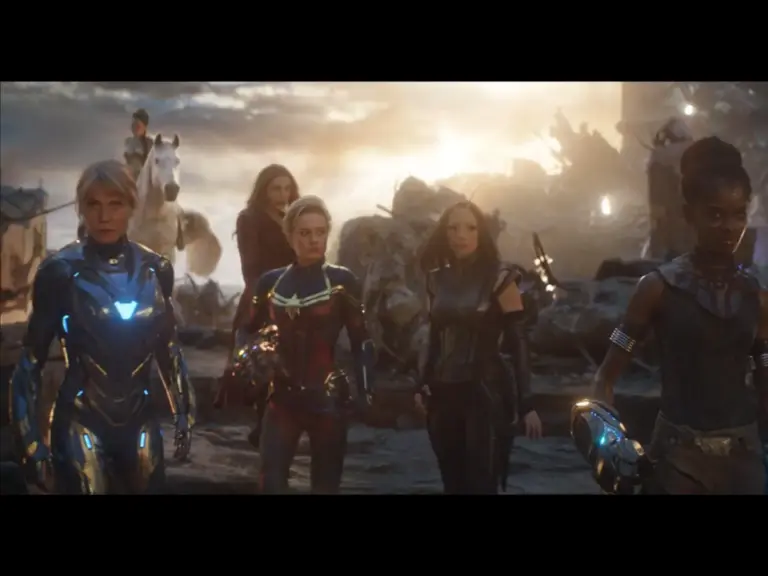 Four women superheroes in futuristic armor stand determined in a battle-scarred landscape at sunset, exuding intense focus and strength.