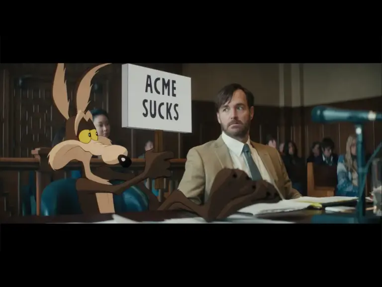Wile E. Coyote and his lawyer sitting sitting side by side in the Coyote Vs. Acne trailer. Wile E. Coyote holds up a sign that says "Acme Sucks,''' while his lawyer looks on.