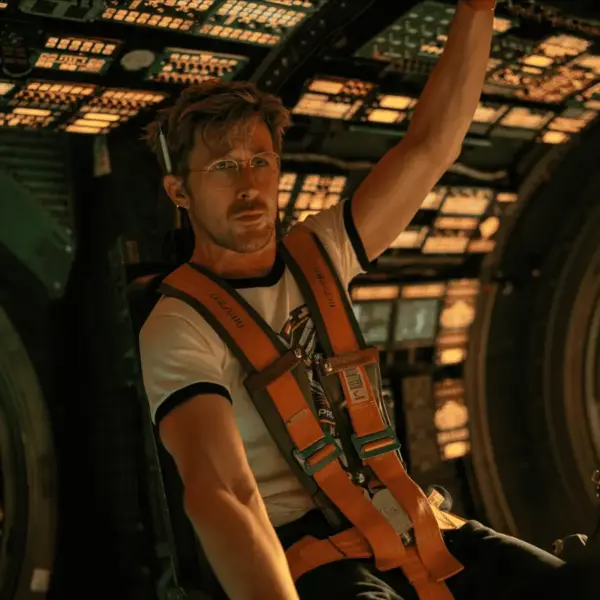 Ryan Gosling Project Hail Mary seated in a spaceship, raising his hands in excitement or celebration.