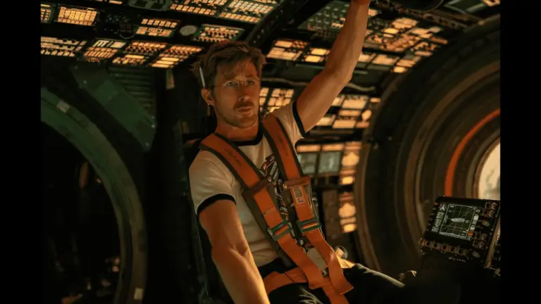 Ryan Gosling Project Hail Mary seated in a spaceship, raising his hands in excitement or celebration.