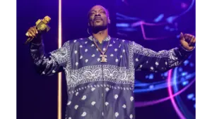 Snoop Biopic — Snoop Dogg performing on stage in a navy bandana-patterned outfit, holding a gold microphone under purple lights.