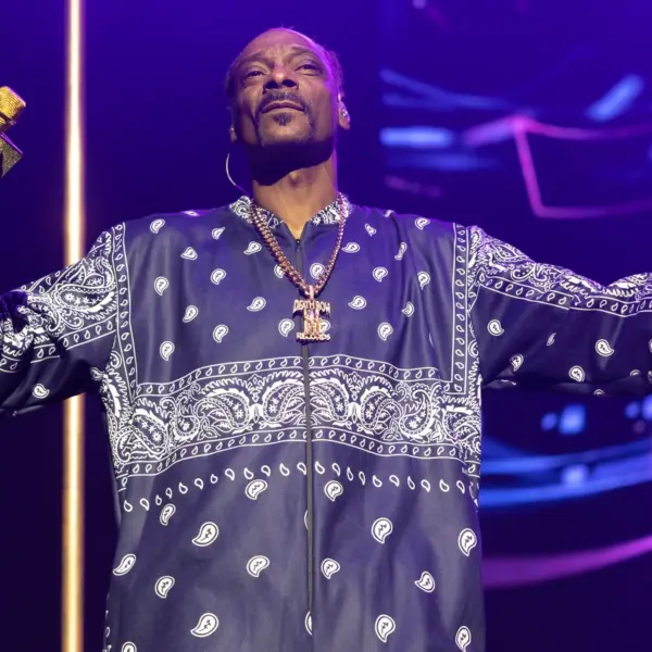 Snoop Biopic — Snoop Dogg performing on stage in a navy bandana-patterned outfit, holding a gold microphone under purple lights.