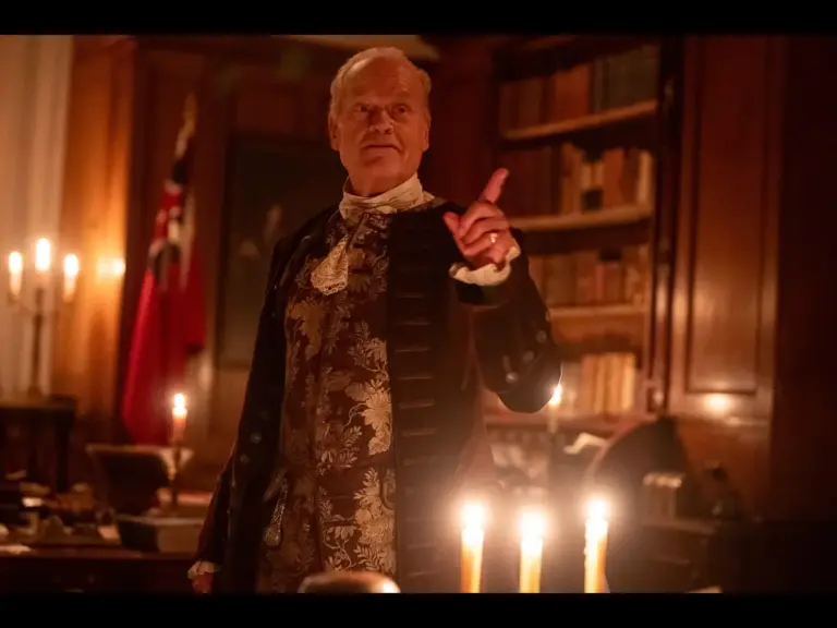 Kelsey Grammer as Lord Fairfax in a historical military uniform riding a horse through a wooded area.