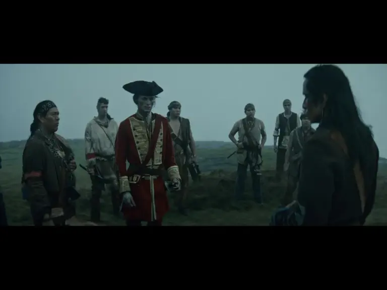 A group of men in historical clothing, including one in a red military uniform and a large hat, stand on a foggy landscape, engaged in a tense conversation.