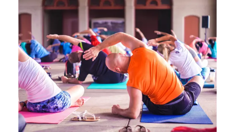 A diverse group of people practice yoga indoors on colorful mats. Stretching to one side, creating a calm and focused atmosphere.