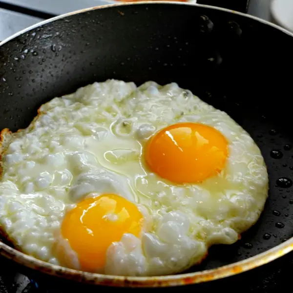 Two eggs sizzling in a frying pan with hot honey caramelizing around the edges, creating sweet‑and‑spicy honey eggs.