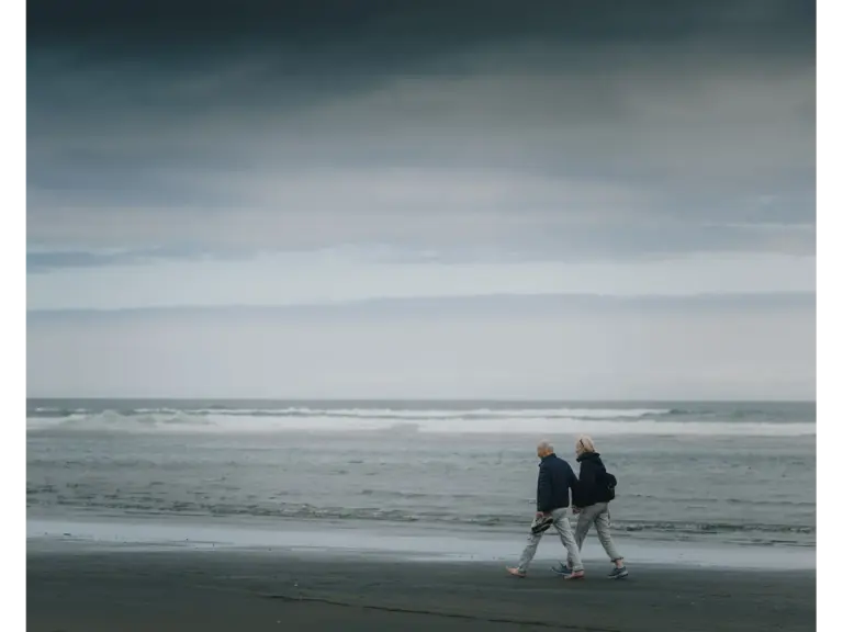 Two people walking on a gloomy beach as dark clouds gather overhead, capturing the moody atmosphere often seen in storm travel.