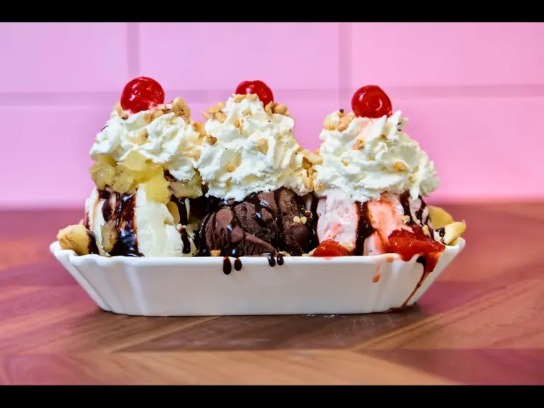Image of a three scoop ice cream sundae with whipped cream and cherries.