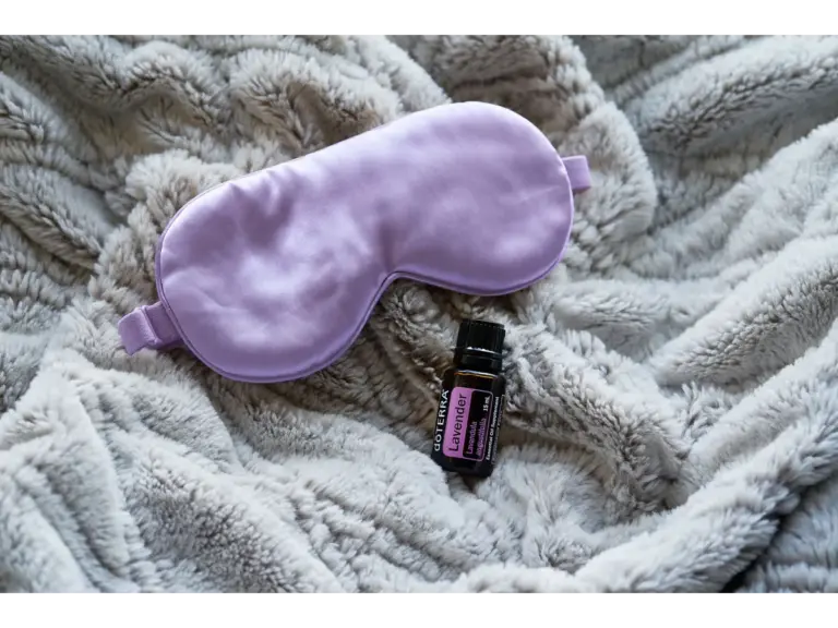 Lavender essential oil alongside a purple sleep mask on a gray blanket promotes relaxation and rest, making it a perfect pairing for calming room sprays.