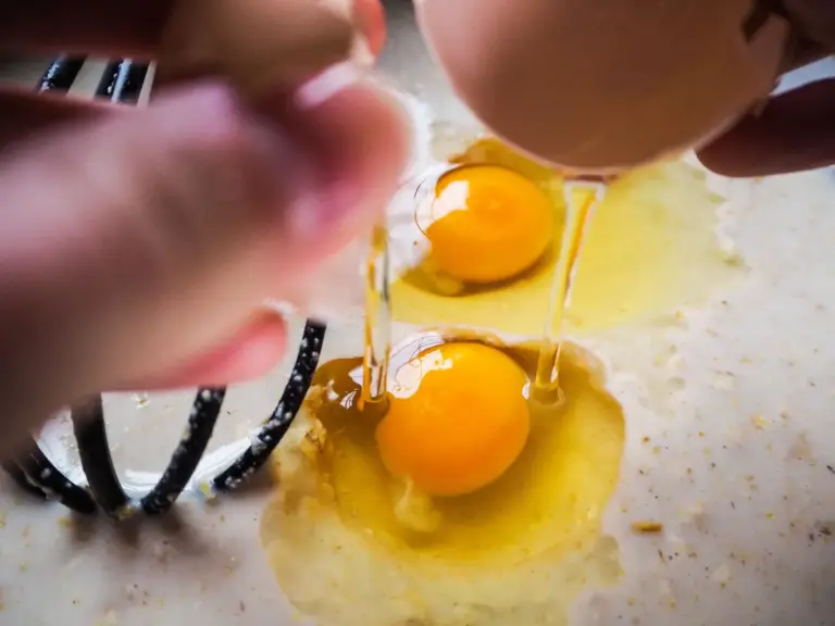 Close‑up of hands skillfully cracking fresh eggs into a bowl, revealing rich yolks ready to become sweet‑and‑spicy honey eggs.