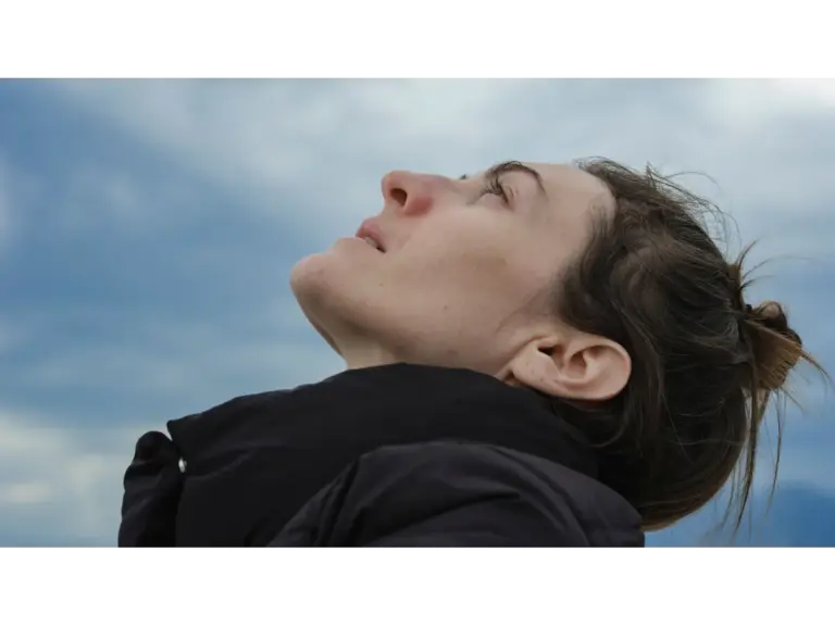 Close‑up side profile of a woman gazing upwards against a blue sky backdrop, capturing a quiet moment shaped by her natural weather intuition.