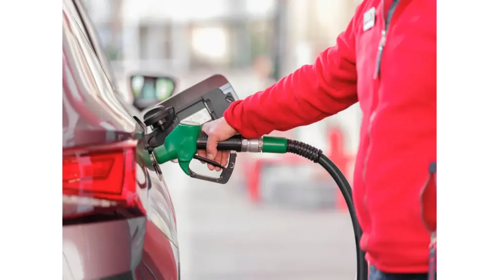 Close-up of a person refueling a car with a green hose at a gas station, capturing the everyday impact of rising gas prices on drivers.