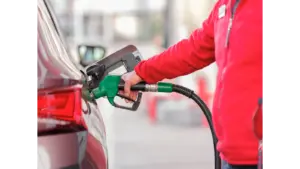 Close-up of a person refueling a car with a green hose at a gas station, capturing the everyday impact of rising gas prices on drivers.