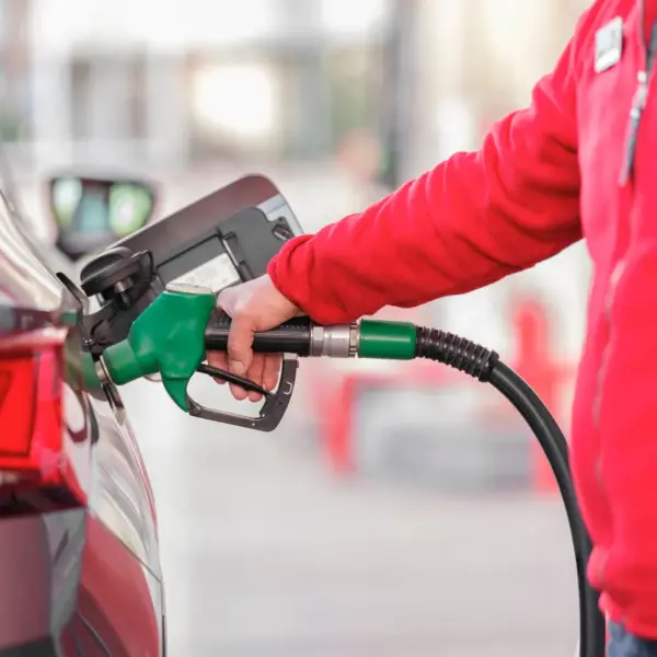 Close-up of a person refueling a car with a green hose at a gas station, capturing the everyday impact of rising gas prices on drivers.