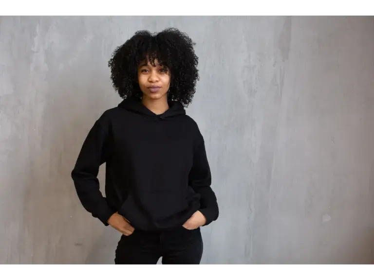 Portrait of a young woman with curly hair wearing a black hoodie, exuding confidence with a natural touch of fashion psychology shaping the mood.