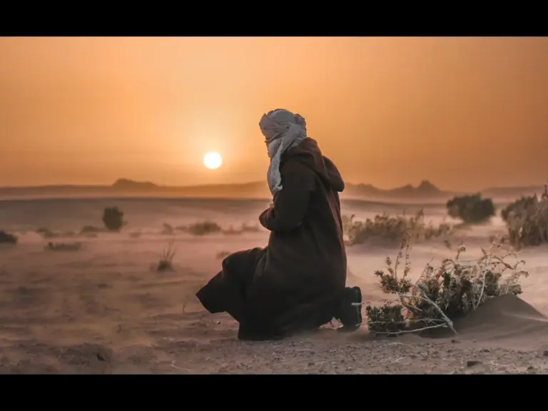 In daily devotional, a man in the desert bends in prayer and faithfulness to God.