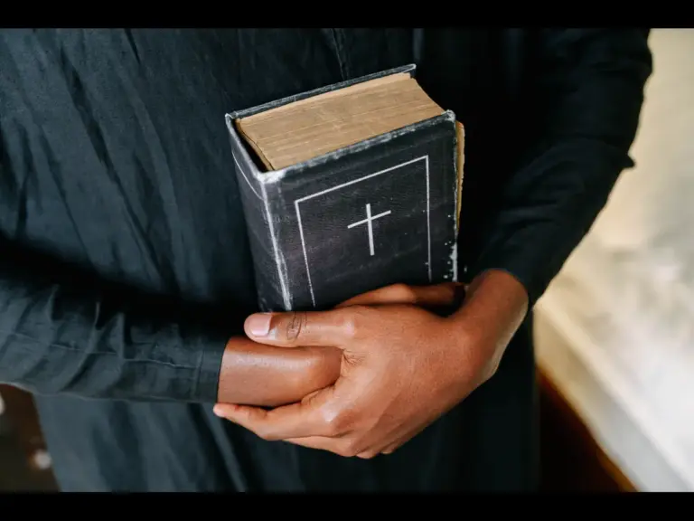 In daily devotional, a man in black robe holds the Bible close to him in reverence to God's word.