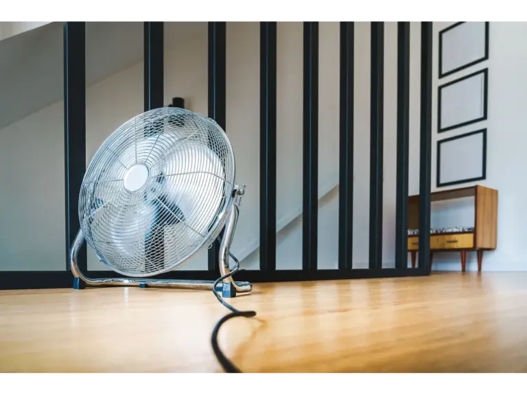A sleek electric fan placed on a wooden floor in a modern indoor setting, providing comfort and home cooling.