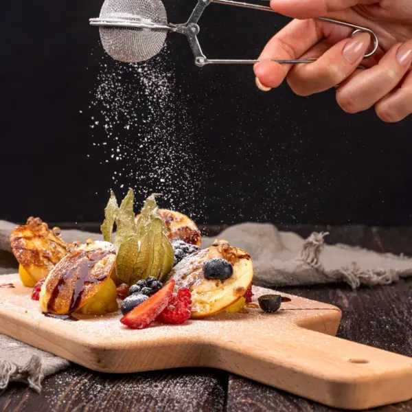 Close-up of pancakes topped with berries and dusted with sugar on a wooden board, capturing the sweet, cozy spirit of the butter craze.