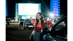 A stylish young woman enjoys a night at the drive-in cinema, exuding confidence and elegance during this drive-in revival.