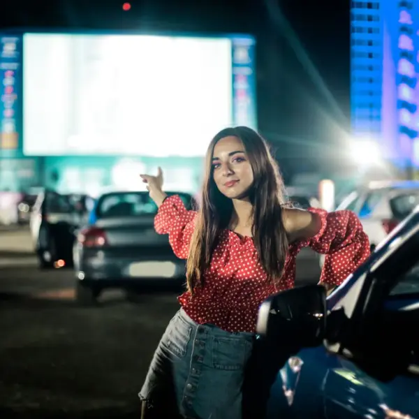 A stylish young woman enjoys a night at the drive-in cinema, exuding confidence and elegance during this drive-in revival.
