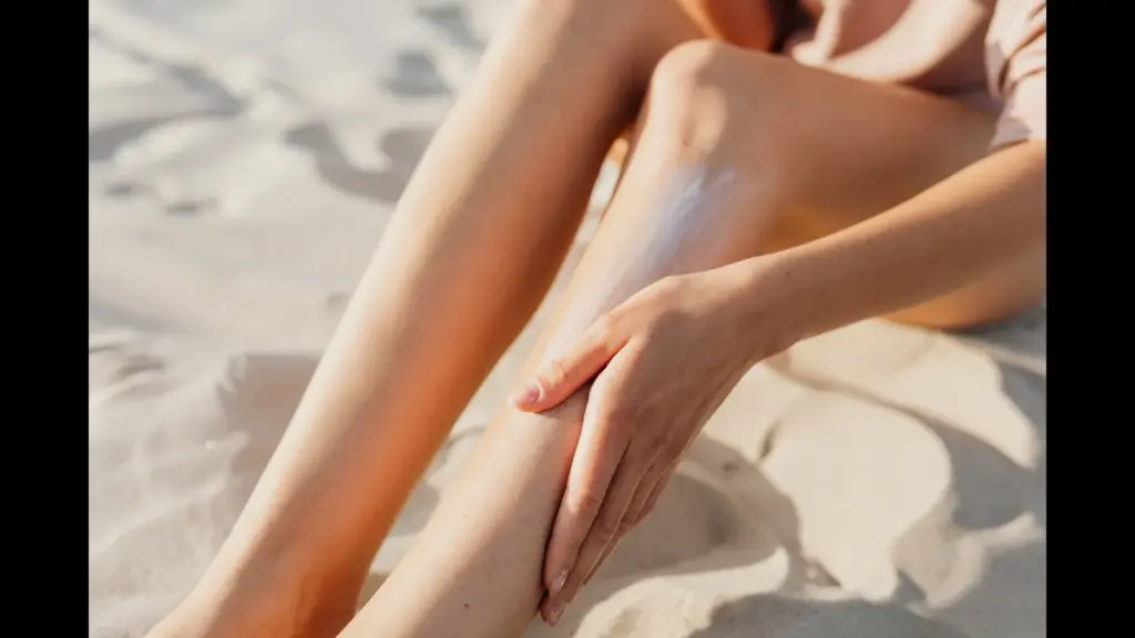A person applying sunscreen to their legs while sitting on the sand, new sunscreen ingredient