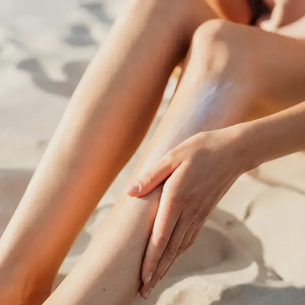 A person applying sunscreen to their legs while sitting on the sand, new sunscreen ingredient