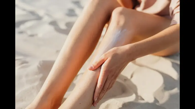 A person applying sunscreen to their legs while sitting on the sand, new sunscreen ingredient
