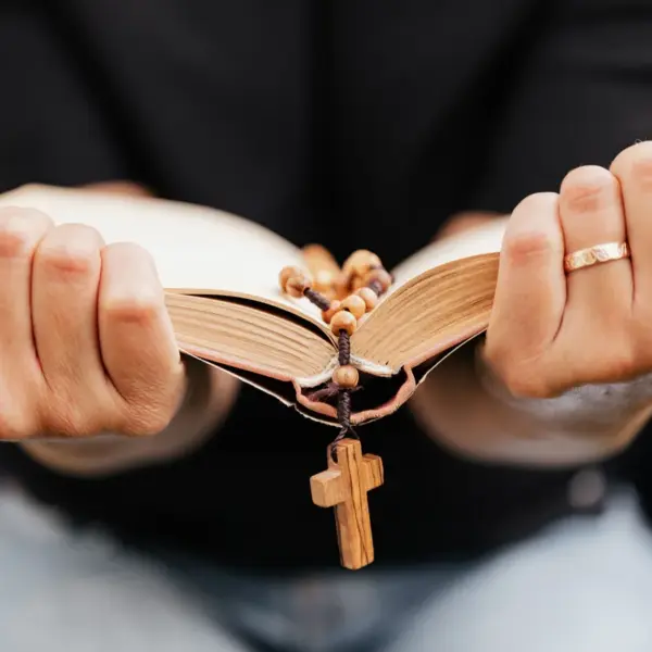 In daily devotional, a woman grasps an open Bible with a cross hanging in its center.