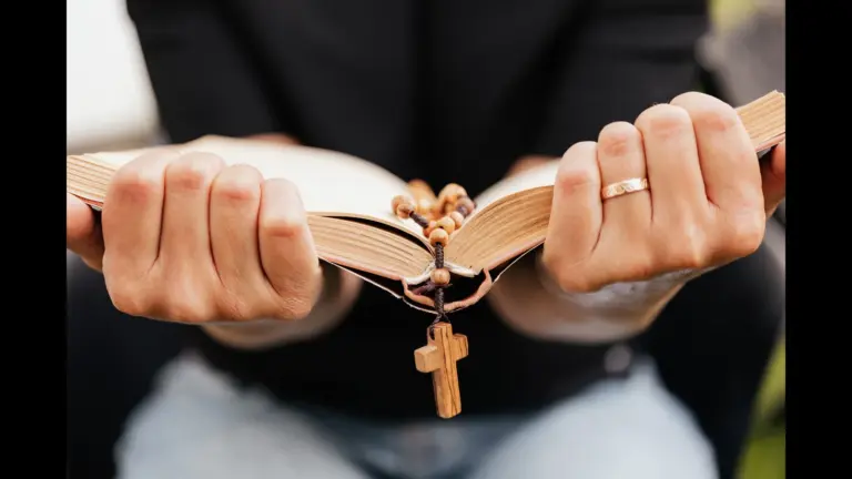 In daily devotional, a woman grasps an open Bible with a cross hanging in its center.