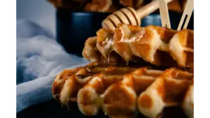 Close-up of warm cinnamon waffles drizzled with honey, served on a black plate for a delicious breakfast treat