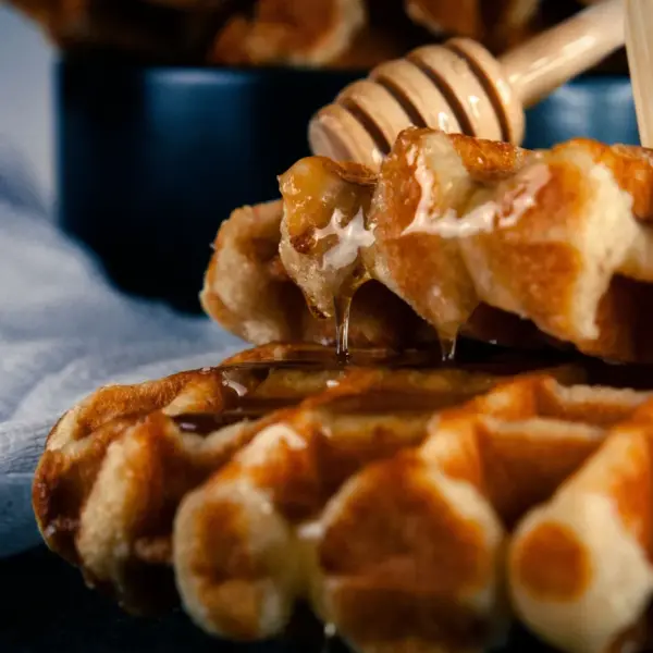 Close-up of warm cinnamon waffles drizzled with honey, served on a black plate for a delicious breakfast treat