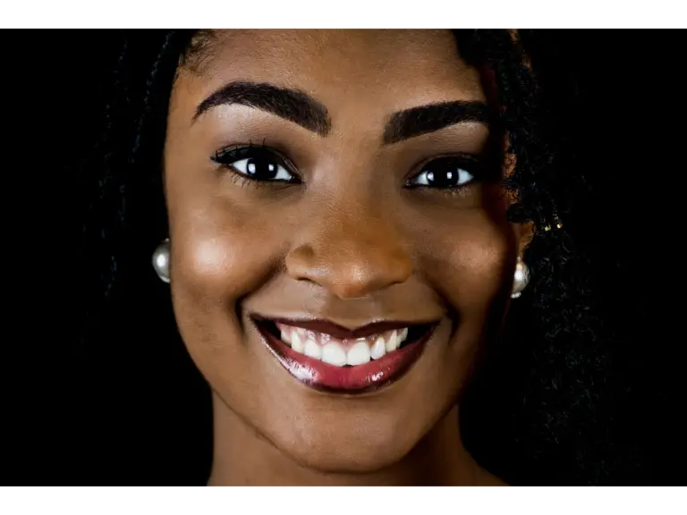 Vibrant portrait of a smiling woman with curly hair against a dark background, glowing with a flawless tone match that highlights her natural beauty.