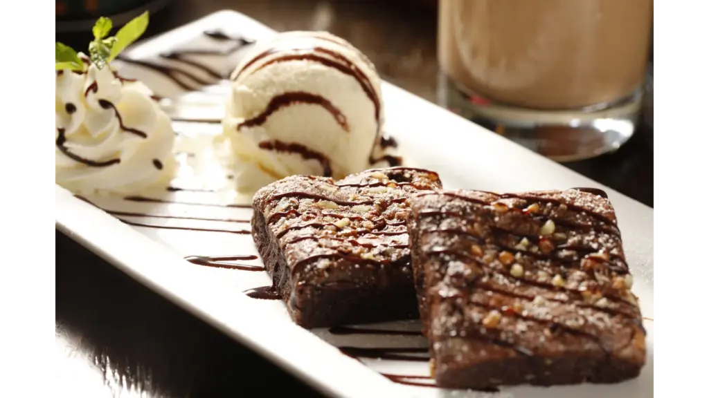 Decadent hot fudge brownies with vanilla ice cream and whipped cream on a white plate