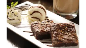 Decadent hot fudge brownies with vanilla ice cream and whipped cream on a white plate