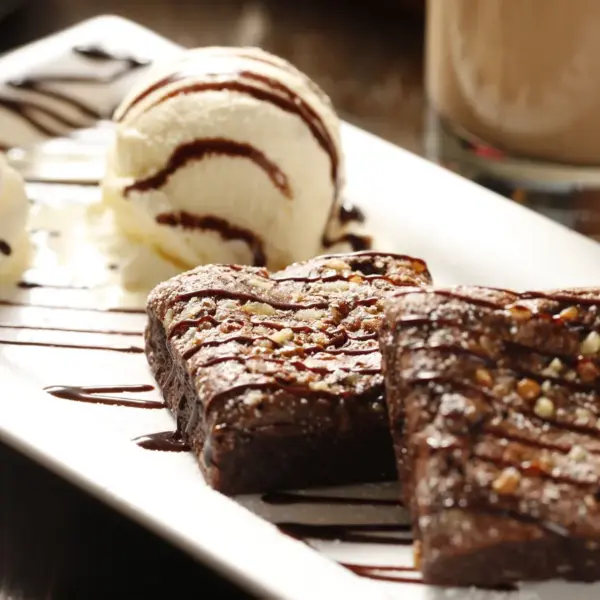 Decadent hot fudge brownies with vanilla ice cream and whipped cream on a white plate