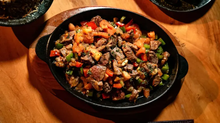 Delicious grilled steak bites with peppers and tomatoes in a hot skillet on wooden table