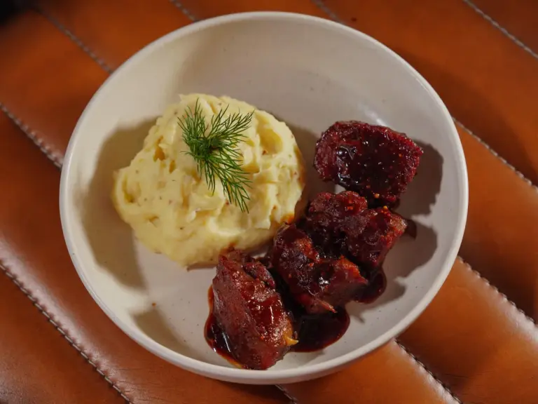 Top view of a bowl with mashed potatoes topped with dill and steak bites in a savory sauce.